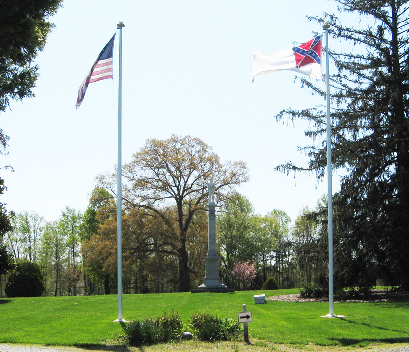 View southeast from the entry drive of the Confederate Cemetery at Spotsylvania Court House. The Confederate Soldiers Monument stands in the center of the cemetery viewed between the flags of the United States and Confederate States.